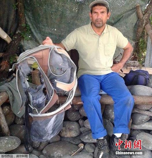 圖為當?shù)貢r間7月30日，留尼旺島上的一名海岸清潔人員展示他找到的一個手提箱的殘骸。